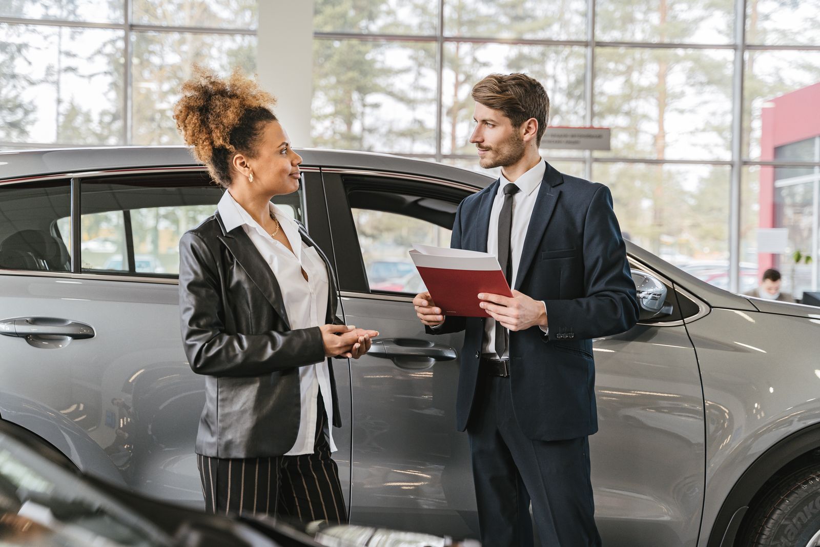 Dealership consultant reviewing paperwork with a customer beside a car in the showroom